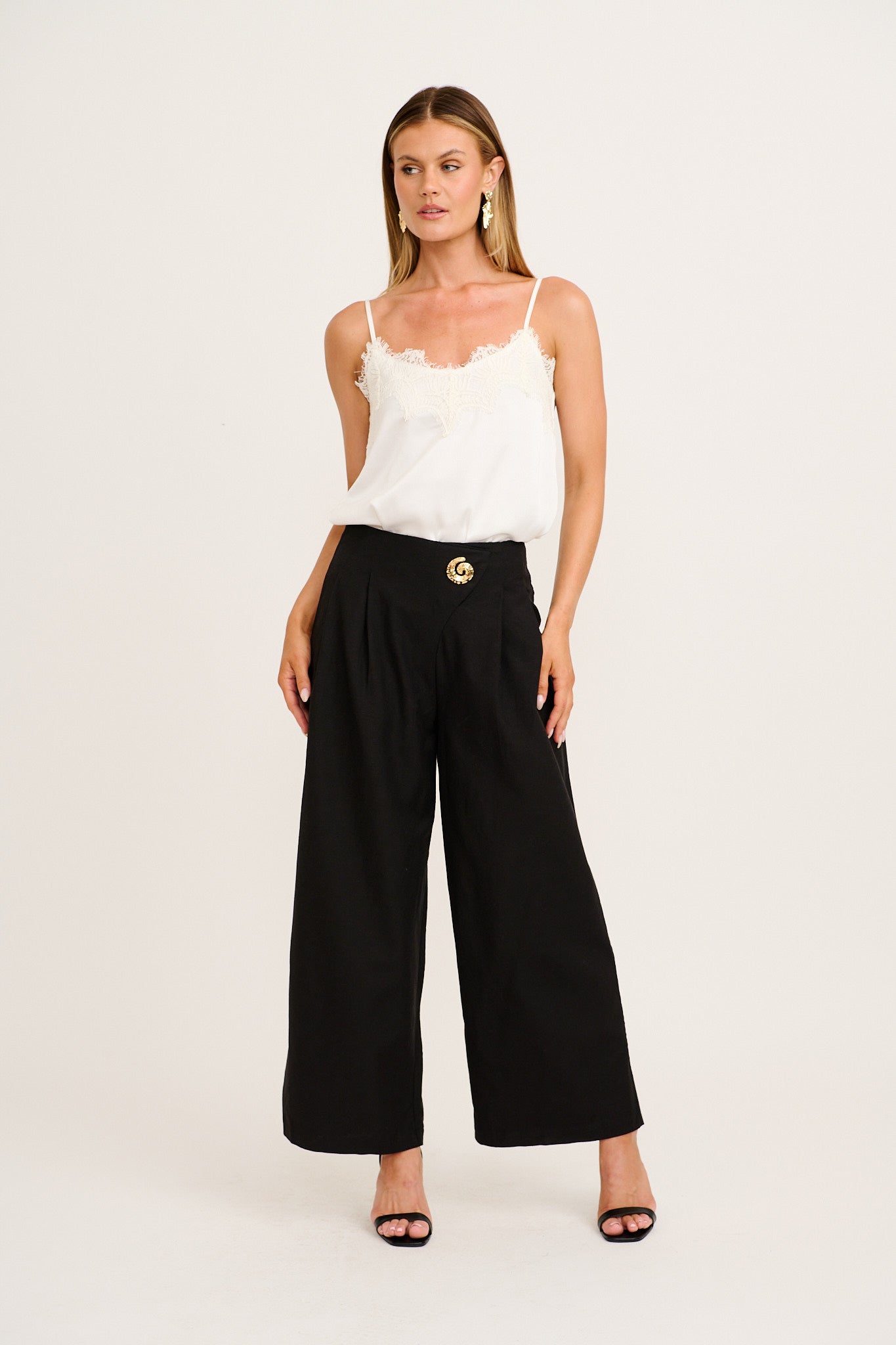 Elements Pant in Black Cotton Linen worn with a white cami, featuring a high-rise wide-leg cut and gold shell brooch detail