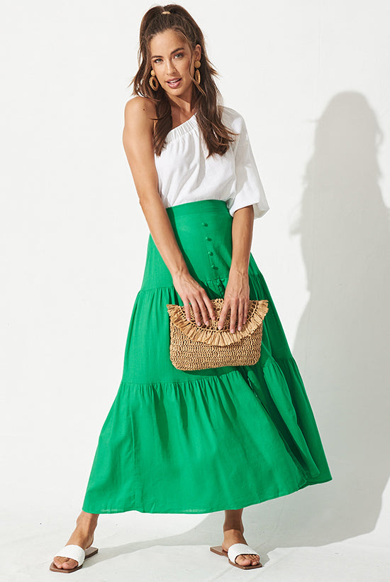 Women in a white, one shouldered top tucked into a bright green maxi skirt.